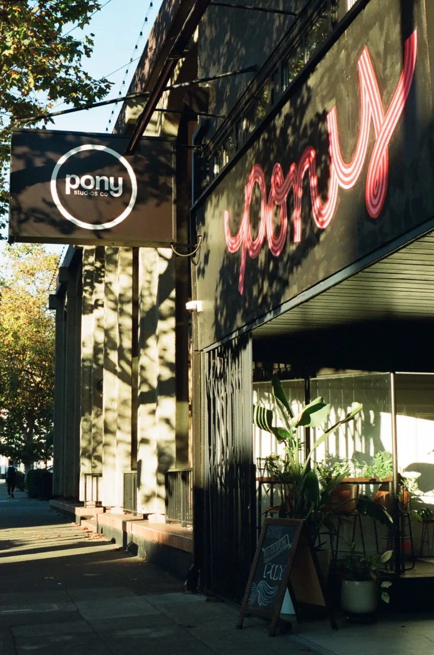 Pony Studios storefront on Telegraph Ave with neon sign and outdoor lounge